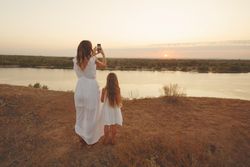 Woman taking photo of sunset on waterfront with little girl