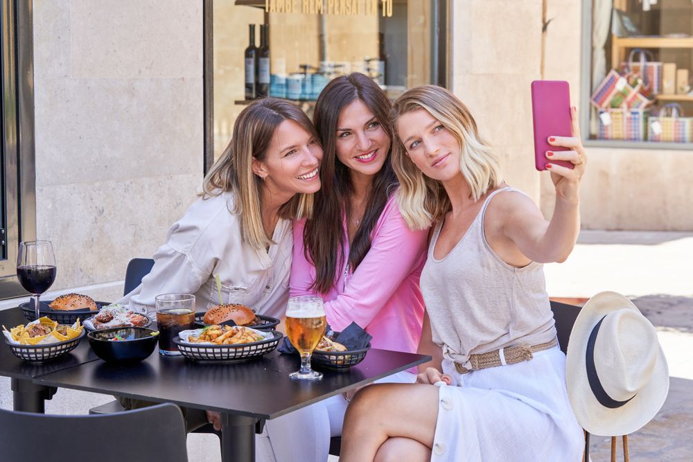 Content female friends taking self portrait while eating in rest