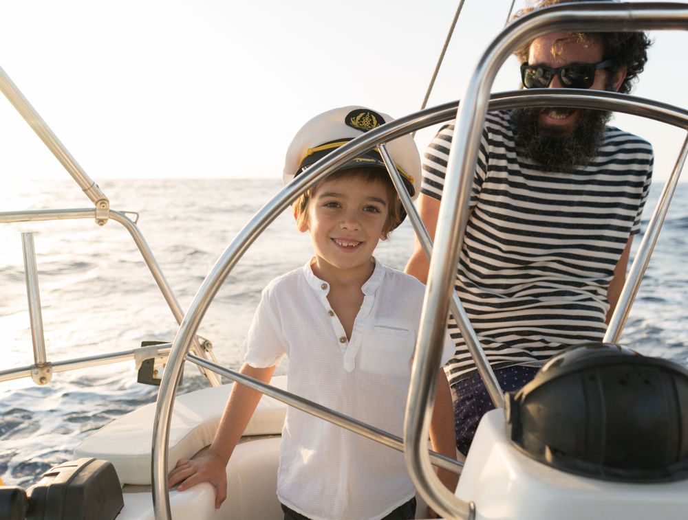 Man with boy holding steering wheel on yacht on water