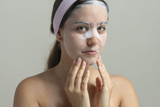 Young woman looking at camera while wearing a hydrating sheet mask for a home spa facial