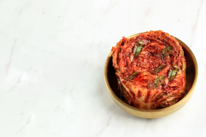 Brass pot of kimchi on marble table with space for text