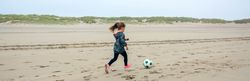 Little girl playing soccer on the beach