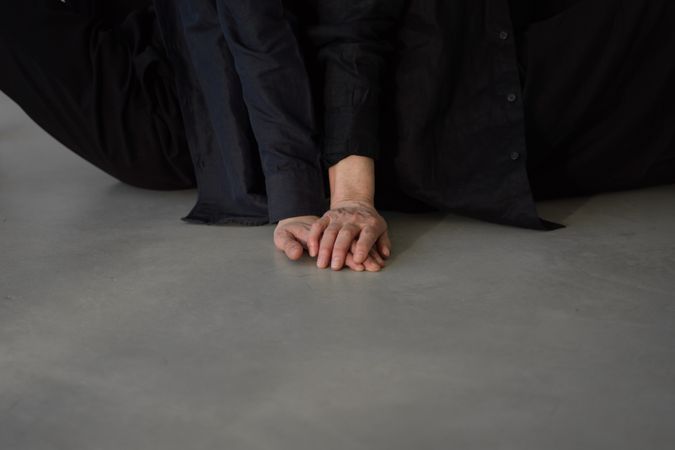 Cropped image of two people in dark outfit touching hands on floor