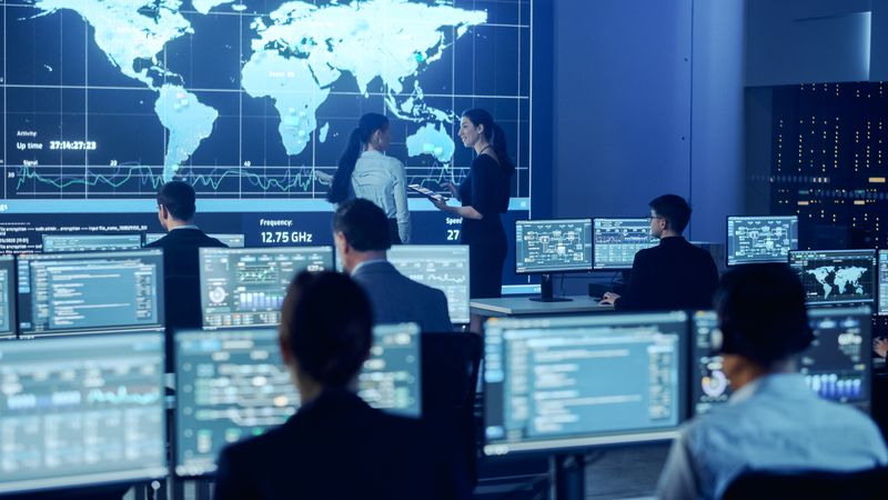 Diverse Team Collaborates in a Futuristic Control Room, Analyzing Global Data on Multiple Screens for Cybersecurity.