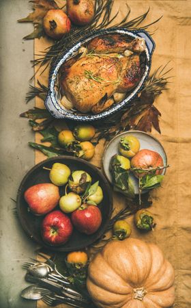 Roast turkey in decorative roasting pan, on table with fall leaves and fruit, vertical composition
