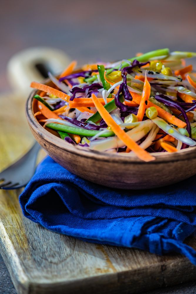 Close up of fresh salad with vegetables in bowl on wooden board with copy space