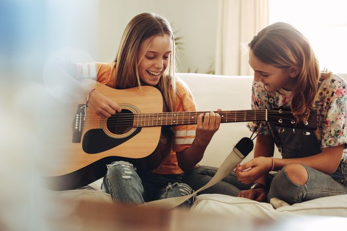 Cheerful girls playing guitar sitting at home