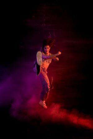 Young woman break dancing in colorful smoke