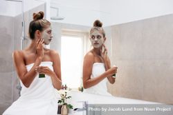 Beautiful female in front of mirror applying facial mask 4MNRrb