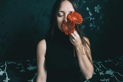 Studio portrait of woman holding gerbera flowers against dark floral background