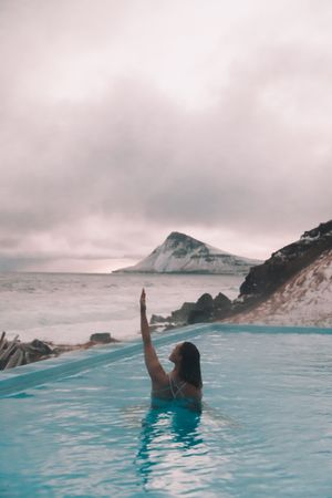 Woman in pool near sea and hills on shore