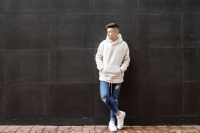 Young man in bright hoodie leaning on dark wall outside