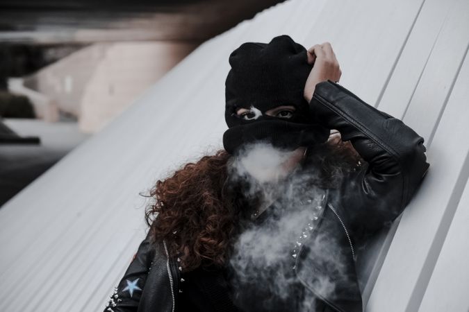 Woman in mask and jacket smoking on street