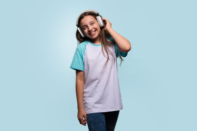 Girl wearing headphones, standing casually and enjoying music.