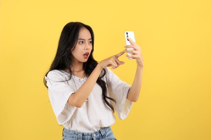 Amazed Surprised Young Asian Toman Stares at Smartphone