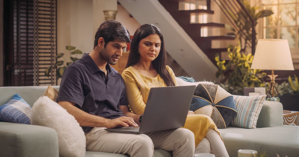 Adorable Young Indian Couple Using Laptop, Sitting on Home Sofa.