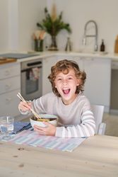 Cheerful boy eating Asian ramen at home