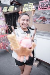A young Hispanic woman is smiling holding a traditional ice cream in front of a street market stall