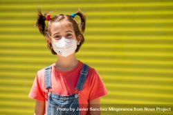 Cute child in protective mask against a yellow wall 5XxjG5