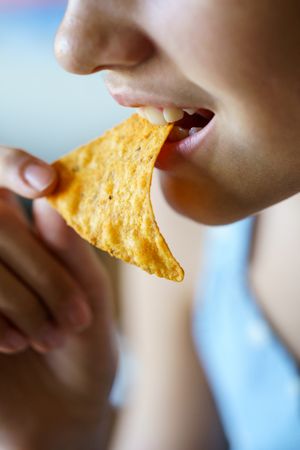 Close up of anonymous teenage girl eating crunchy Mexican tortilla chip