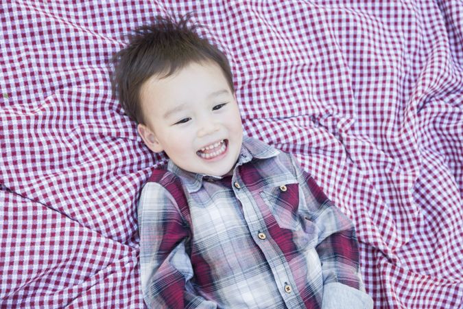 Cute Young Biracial Boy Laughing On Picnic Blanket