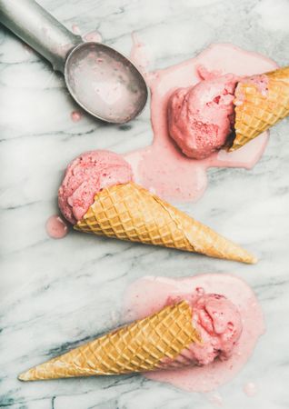 Homemade strawberry yogurt ice cream in cones laying on marble counter top, vertical composition