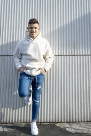 Portrait of young man with hands in pocket leaning on wall outside