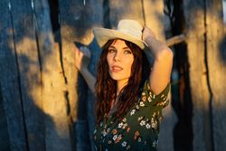 Female brunette leaning against wooden fence outside at magic hour