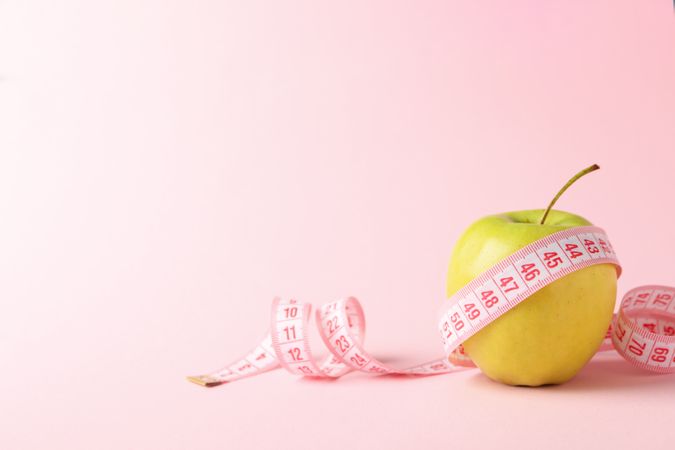 Measuring tape with apple on pink background, weight loss