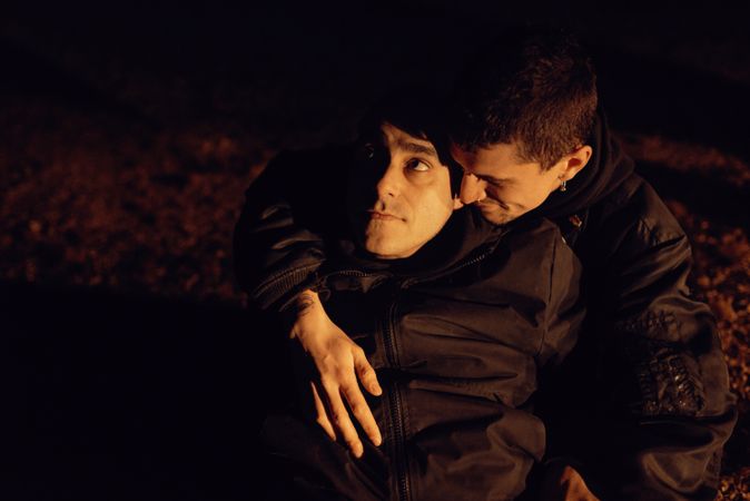 Men hugging and sitting on ground on field at night