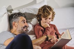Father and son reading interesting book while lying on bed