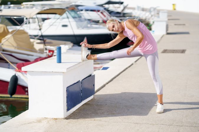 Older female in pink athletic wear stretching her legs before workout