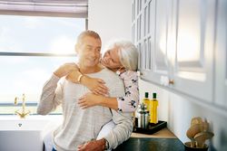 Happy mature woman holder her husband from behind in the kitchen