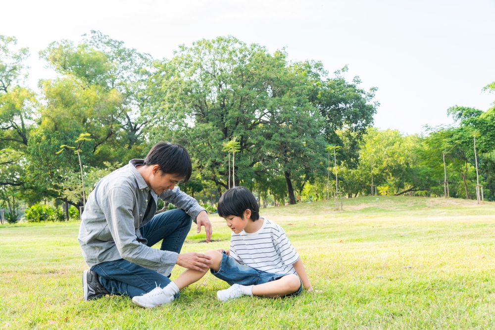 Supporting dad checking on boy leg at the park