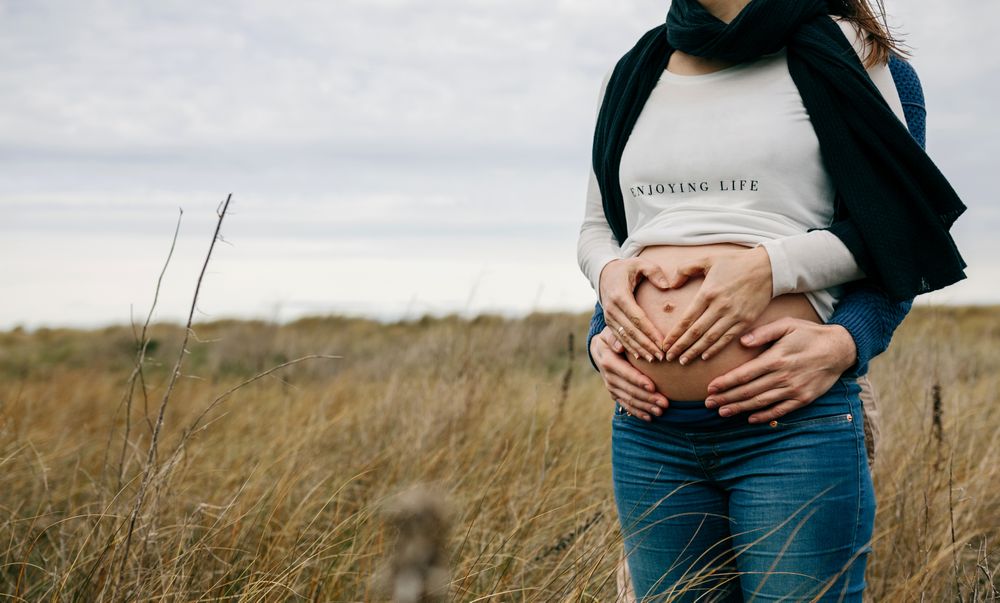 Pregnant person making heart with hands on naked belly with partner