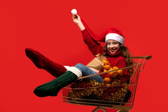 Teen girl in Santa hat in shopping cart with oranges.