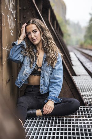 Woman wearing blue denim jacket and bra sitting while touching her hair