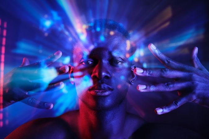 Calm Black man holding hands near face in neon lights