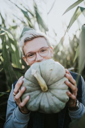 Blonde man with eyeglasses holding green pumpkin