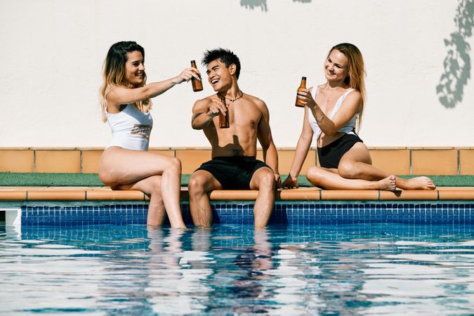 two young women and an asiatic man drinking beer by the pool