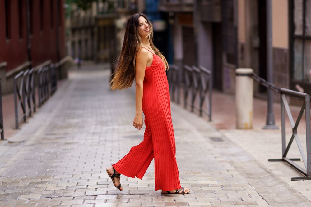 A Fashionable Woman Dressed in a Stunning Red Dress is Walking Through a Lively Urban Alley