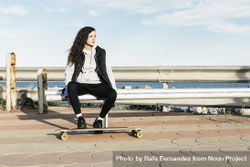 Teenage girl sitting on a bench with her feet on the longboard in front of the sea 4mWZnX