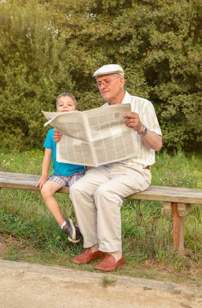 Man in cap and bored child reading newspaper outdoors