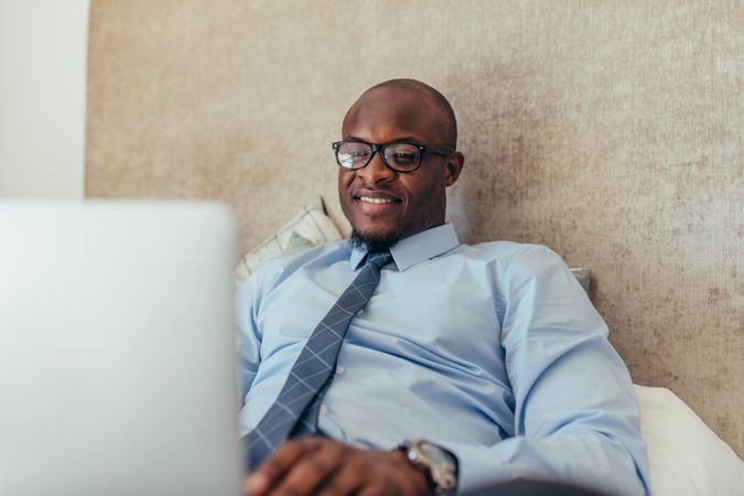 Smiling man working on laptop relaxing on bed