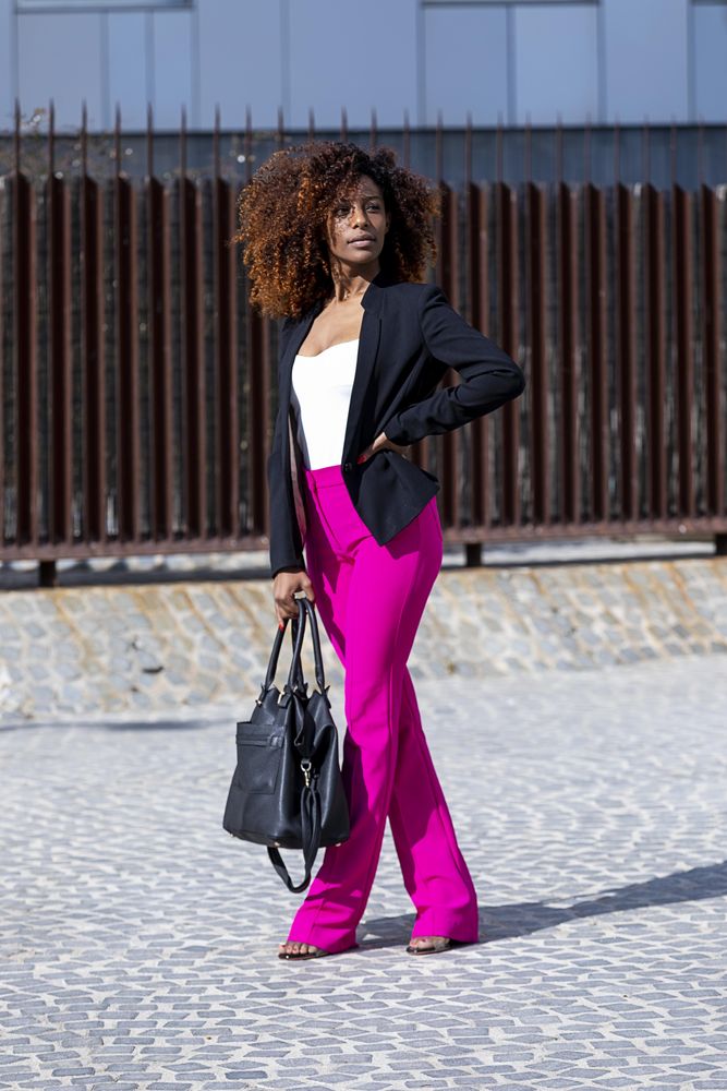 Full body shot of Black female in bright pink trousers standing outside with hand on hip
