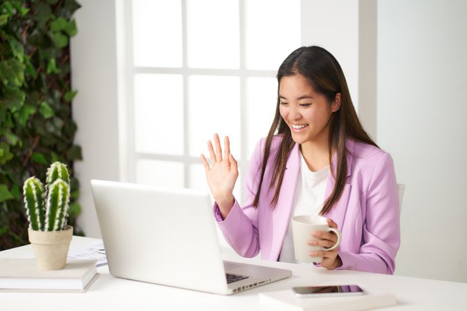 a young asian woman smiling talking on a video call in the coworking room having coffee