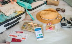 Woman preparing suitcase for vacation and mobile phone with covid green pass