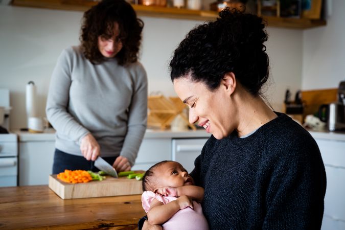 Newborn daughter with smiling mother in kitchen