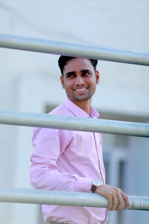 Smiling man in pink shirt standing beside railing outdoor