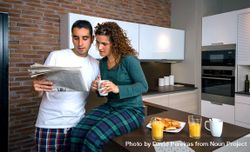 Couple in pajamas reading paper together in kitchen at breakfast time with coffee and orange juice 5pX7y5